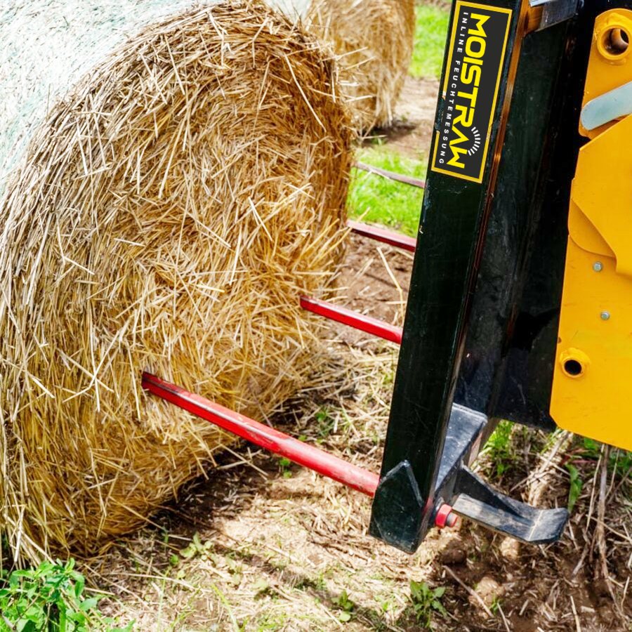 Ballengabel mit MOISTRAW-Aufkleber sticht in einen Strohrundballen